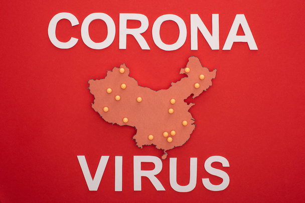 Top view of china map with yellow push pins and coronavirus lettering on red background - 写真・画像