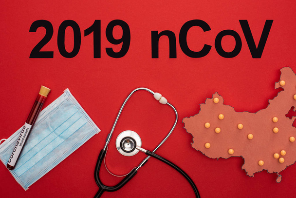 Felülnézet 2019 ncov betűk, elrendezés a porcelán térkép kémcsővel orvosi maszk és sztetoszkóp piros háttér - Fotó, kép