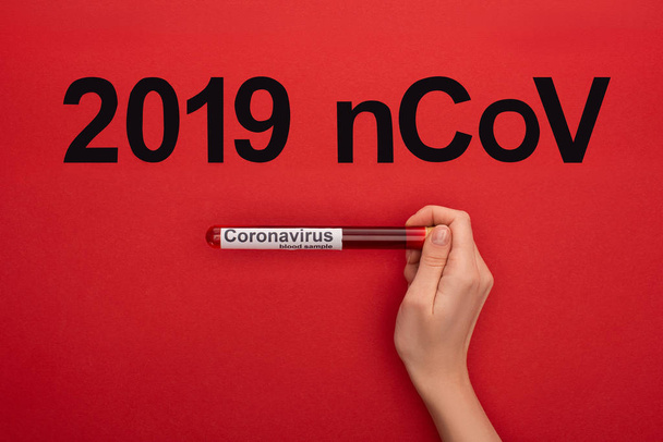 Top view of woman holding test tube with blood sample and 2019 ncov lettering on red surface, panoramic shot - Zdjęcie, obraz