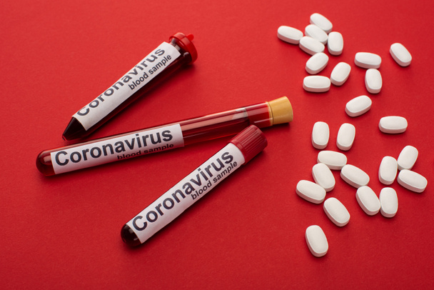 Vista de cerca de pastillas y tubos de ensayo con muestras de sangre y letras de coronavirus sobre fondo rojo
 - Foto, Imagen