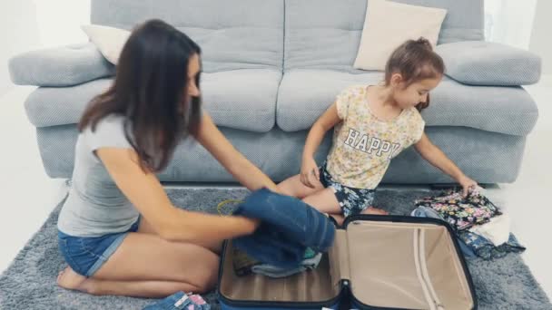 Mom is packing a huge blue suitcase. Little girl is hepling her. Getting ready for travel. 4K. - Materiał filmowy, wideo