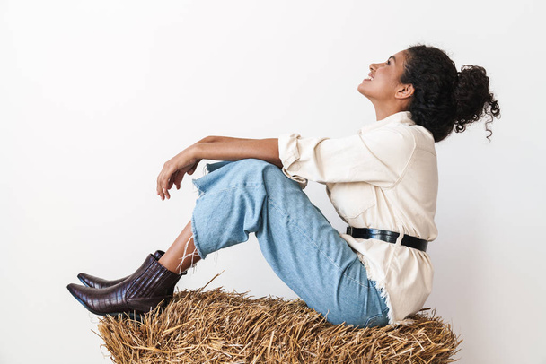 Beautiful smiling young african cowgirl sitting on a haystack - Foto, afbeelding