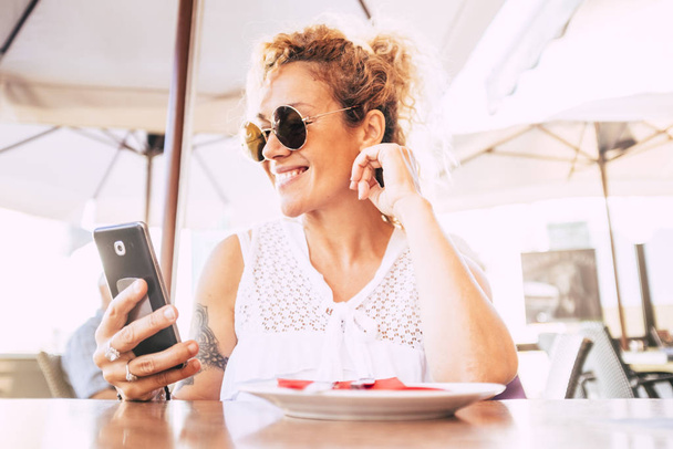 Hermosa y feliz modelo adulto mujer utilizar el teléfono celular moderno en el restaurante con conexión wifi
  - Foto, imagen