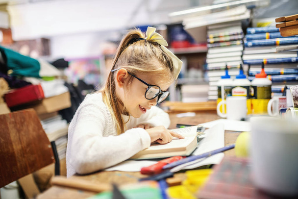 Suloinen valkoihoinen vaalea tyttö, jolla on poninhäntä ja silmälasit, istuu kirjakaupassa ja lukee jännittävää kirjaa.
. - Valokuva, kuva