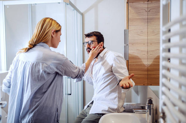 Angry blond woman slapping her husband in the face because of his attitude.Bathroom interior. - Photo, Image