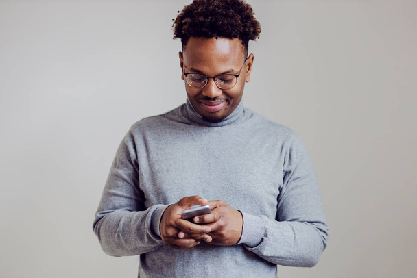 Happy attractive african american man standing and typing message on smart phone. - 写真・画像