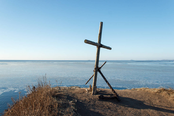 Das alte Denkmal ist ein Holzkreuz und ein alter rostiger Anker auf einer Klippe am äußersten Ende des Kap Tobizin auf der russischen Insel Wladiwostok. - Foto, Bild