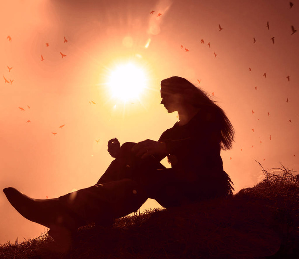 Freedom and feel good concept. Copy space of silhouette woman sitting above hill  on sunset sky  colorful  light and birds fly background. - Photo, Image
