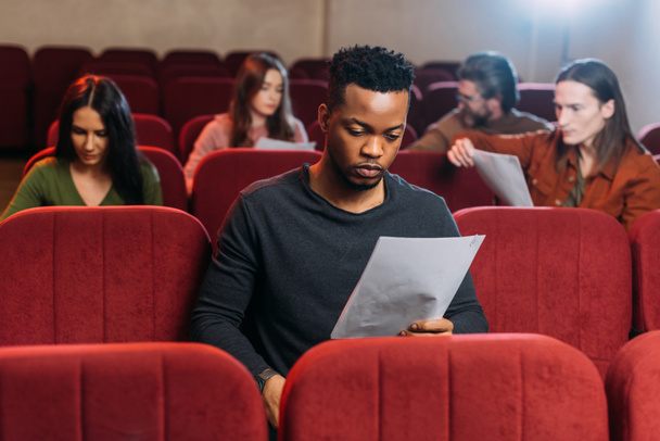Afrykański amerykański aktor czytający scenariusz na fotelach w teatrze - Zdjęcie, obraz