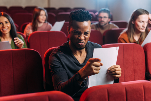 Wütender afrikanisch-amerikanischer Schauspieler probt auf roten Stühlen mit Schauspielern - Foto, Bild
