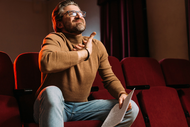emotioneel theaterregisseur met scenario op stoelen in theater - Foto, afbeelding