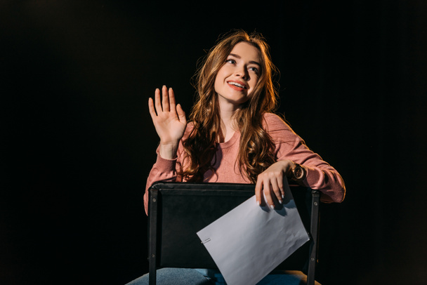 cheerful young actress with scenario sitting on chair on stage in theatre - Zdjęcie, obraz