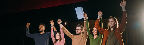 panoramische opname van gelukkige acteurs en actrices met handen omhoog op het podium - Foto, afbeelding