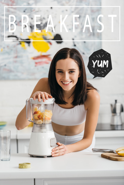 Selective focus of attractive sportswoman smiling at camera while preparing smoothie in blender near breakfast illustration - Fotoğraf, Görsel