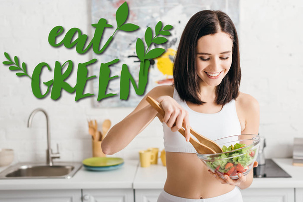 Attractive fit sportswoman smiling while mixing salad on kitchen, eat green illustration - Photo, Image