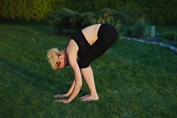Молода жінка робить йогу в медитаційній позі на килимку в саду
. - Фото, зображення