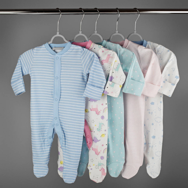 Farbiges Kleidungsset für Neugeborene, das an einem Kleiderbügel hängt. Das Konzept von Kleidung, Mutterschaft und Neugeborenem. - Foto, Bild