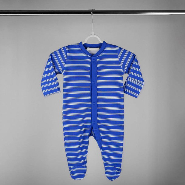 Dunkelblau gestreifte Kleidung für ein Neugeborenes, das an einem Kleiderbügel hängt. Das Konzept von Kleidung, Mutterschaft und Neugeborenem. - Foto, Bild