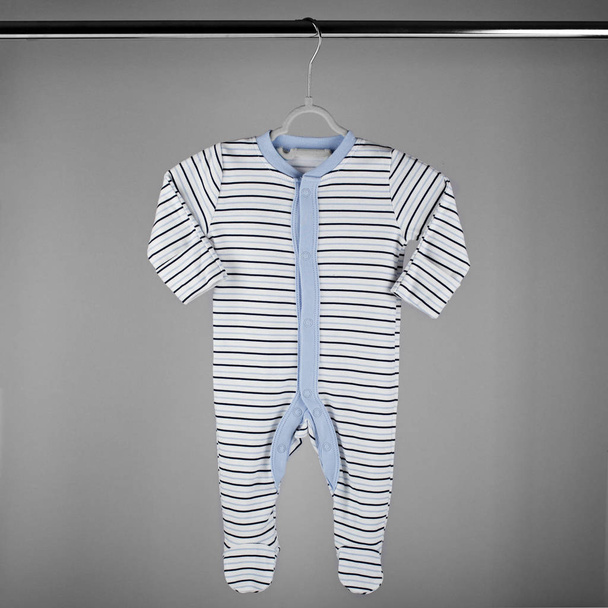 Blaugestreifte Kleidung für ein Neugeborenes, das an einem Kleiderbügel hängt. Das Konzept von Kleidung, Mutterschaft und Neugeborenem. - Foto, Bild