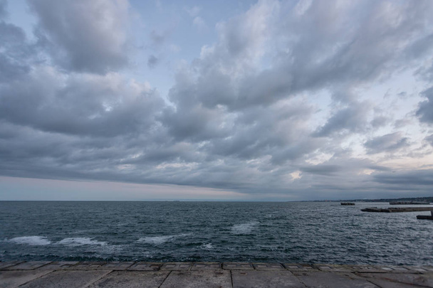 Gloomy, not bright sunset on the sea. Slabs and stones, shore re - Φωτογραφία, εικόνα