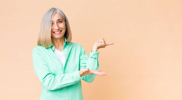 middle age cool woman smiling cheerfully and pointing to copy space on palm on the side, showing or advertising an object - Photo, image