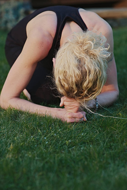 Bahçedeki bir paspasın üzerinde meditasyon pozisyonunda yoga yapan genç bir kadın.. - Fotoğraf, Görsel