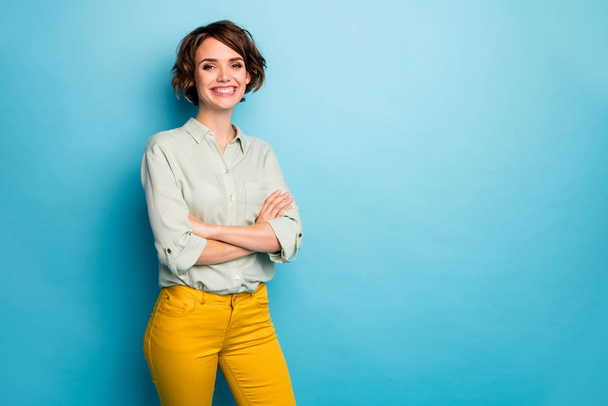 Photo of cool attractive business lady short hairstyle friendly beaming smiling arms crossed good mood wear casual green shirt yellow pants isolated blue color background - Foto, Bild