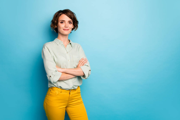 Photo of attractive pretty business lady short hairstyle friendly smiling responsible person arms crossed wear casual green shirt yellow pants isolated blue color background - Фото, зображення