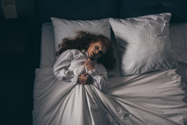 κορυφαία άποψη του παραφυσικό gothic κορίτσι σε νυχτικό ξαπλωμένη στο κρεβάτι - Φωτογραφία, εικόνα