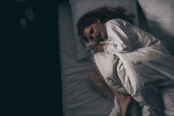 κορυφαία άποψη του δαιμονική εμμονή γυναίκα σε νυχτικό που βρίσκεται στο κρεβάτι - Φωτογραφία, εικόνα
