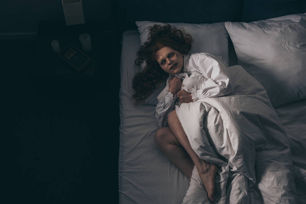 vue de dessus de la femme démoniaque en chemise de nuit couchée dans le lit
 - Photo, image