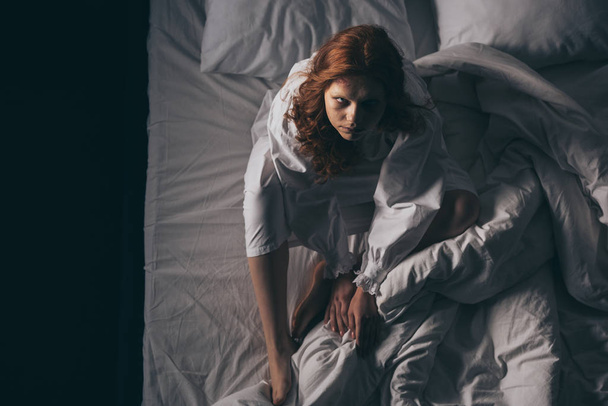 γενικά άποψη της δαιμονικής παραφυσική γυναίκα σε νυχτικό κάθεται στο κρεβάτι - Φωτογραφία, εικόνα
