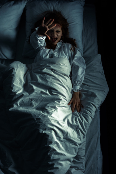 top view of evil girl in nightgown screaming and gesturing while lying in bed - Photo, Image