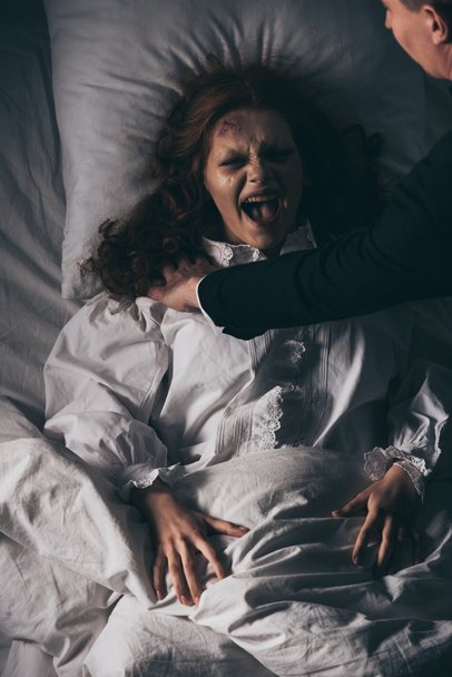 εξορκιστής κρατώντας ουρλιάζοντας εμμονή κορίτσι στο κρεβάτι - Φωτογραφία, εικόνα