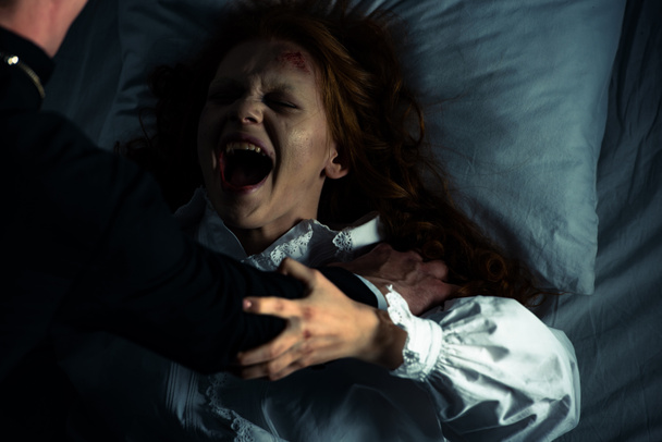 exorcista drží křičící posedlou dívku v posteli - Fotografie, Obrázek