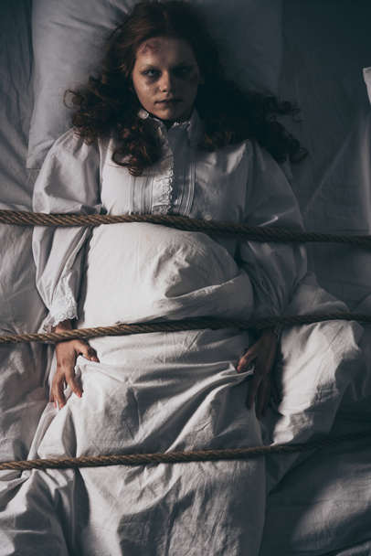 Besessenes Mädchen im Nachthemd mit Seil im Bett gefesselt - Foto, Bild
