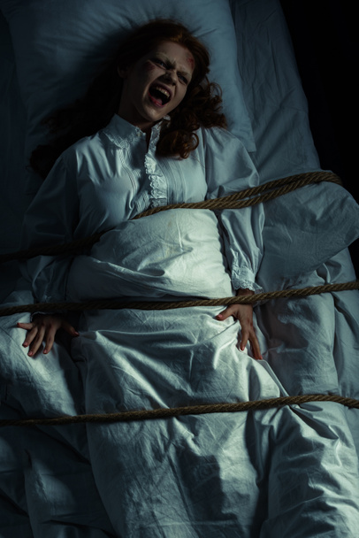 παθιασμένη φωνάζοντας γυναίκα με νυχτικό δεμένο με σχοινί στο κρεβάτι - Φωτογραφία, εικόνα
