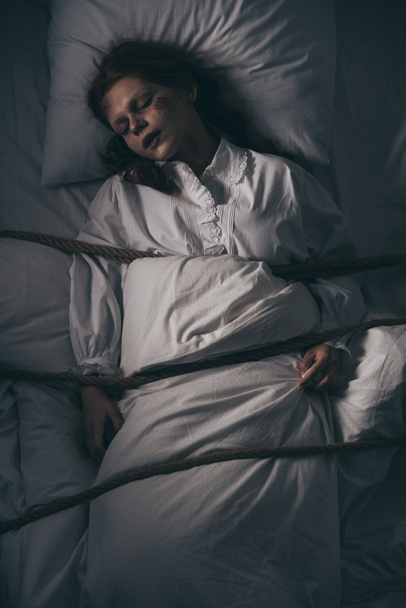 démoni megszállott alvó lány hálóingben kötéllel az ágyban - Fotó, kép