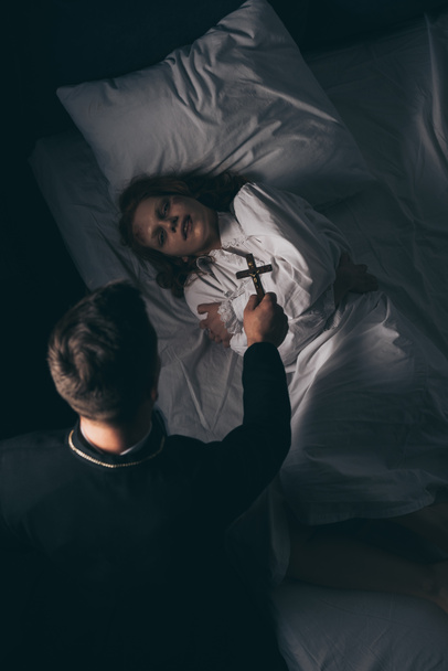 exorcist holding cross over obsessed girl in bed - Fotografie, Obrázek