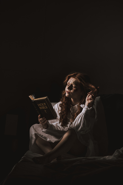 figyelmes démoni nő, aki szent bibliát olvas az ágyon. - Fotó, kép
