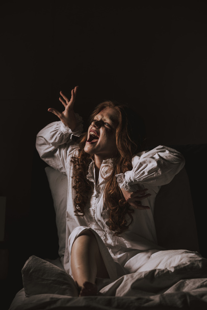 besessenes gruseliges Mädchen im Nachthemd gestikuliert und schreit im Schlafzimmer - Foto, Bild