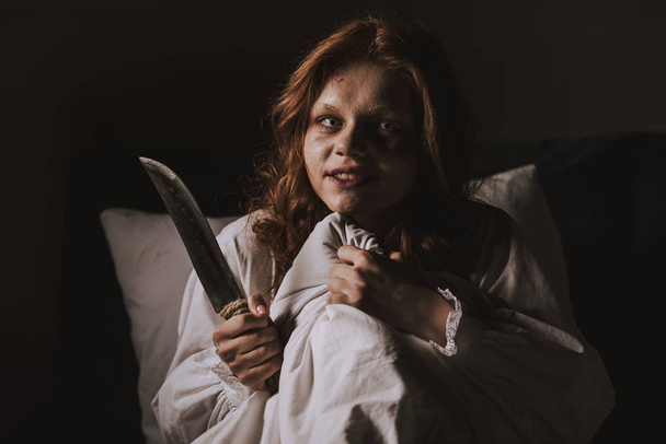 demoniacal girl in nightgown holding knife in bed - Photo, Image