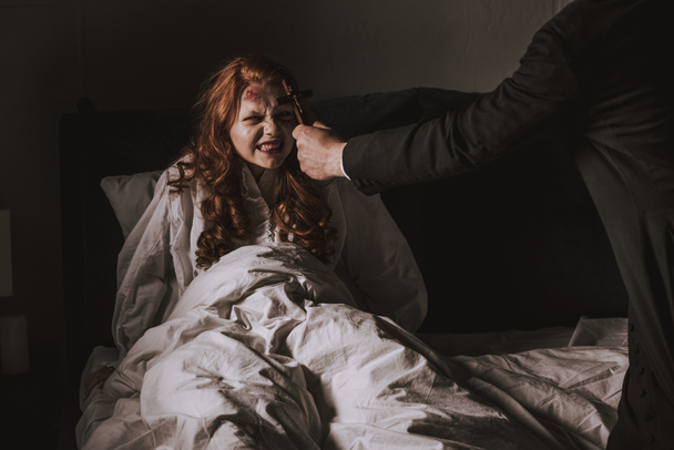 exorcista segurando cruz na frente da menina obcecada na cama
 - Foto, Imagem