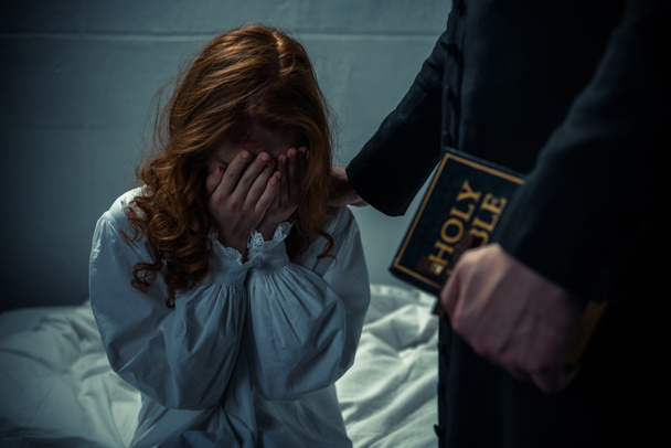 exorcist holding bible and hugging crying girl in bedroom  - Photo, Image