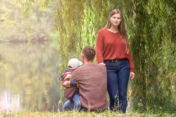 Szczęśliwa rodzina trzyma się za ręce siedząc na zielonym trawniku outdoor parku, mając czas razem. - Zdjęcie, obraz
