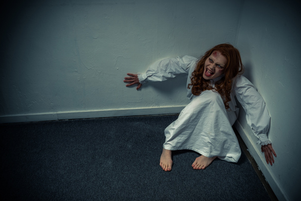 παθιασμένο δαιμονικό κορίτσι με νυχτικό να φωνάζει και να κάθεται κοντά στον τοίχο - Φωτογραφία, εικόνα