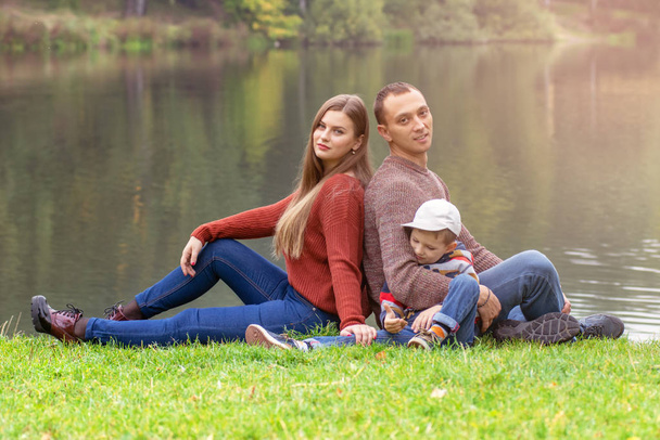 Šťastná rodina drží za ruce sedí na trávníku venkovní park, mají kvalitní čas spolu. - Fotografie, Obrázek