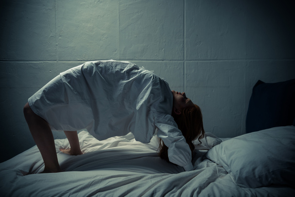 megszállott démoni lány hálóingben, lábakon és karokon áll az ágyon.  - Fotó, kép