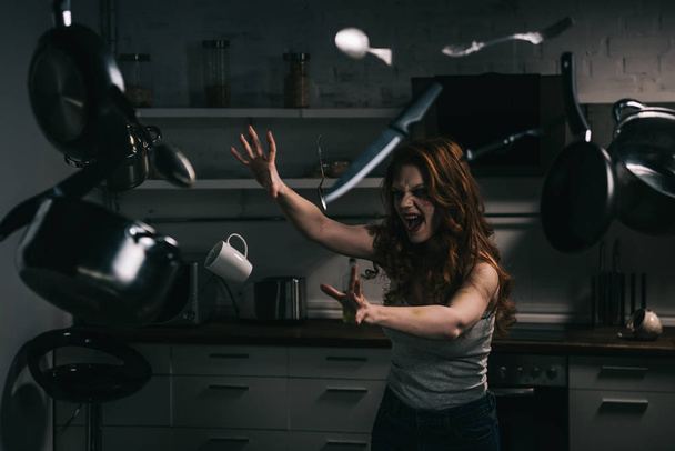 raccapricciante urlando ragazza gesticolando con utensili da cucina levitanti in cucina
 - Foto, immagini