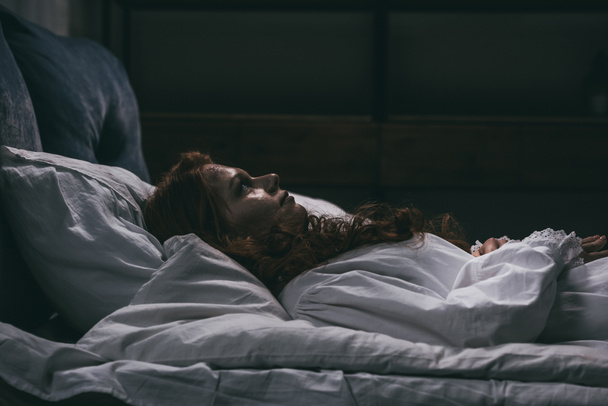 Verrückte dämonische Frau im Nachthemd im Bett liegend - Foto, Bild